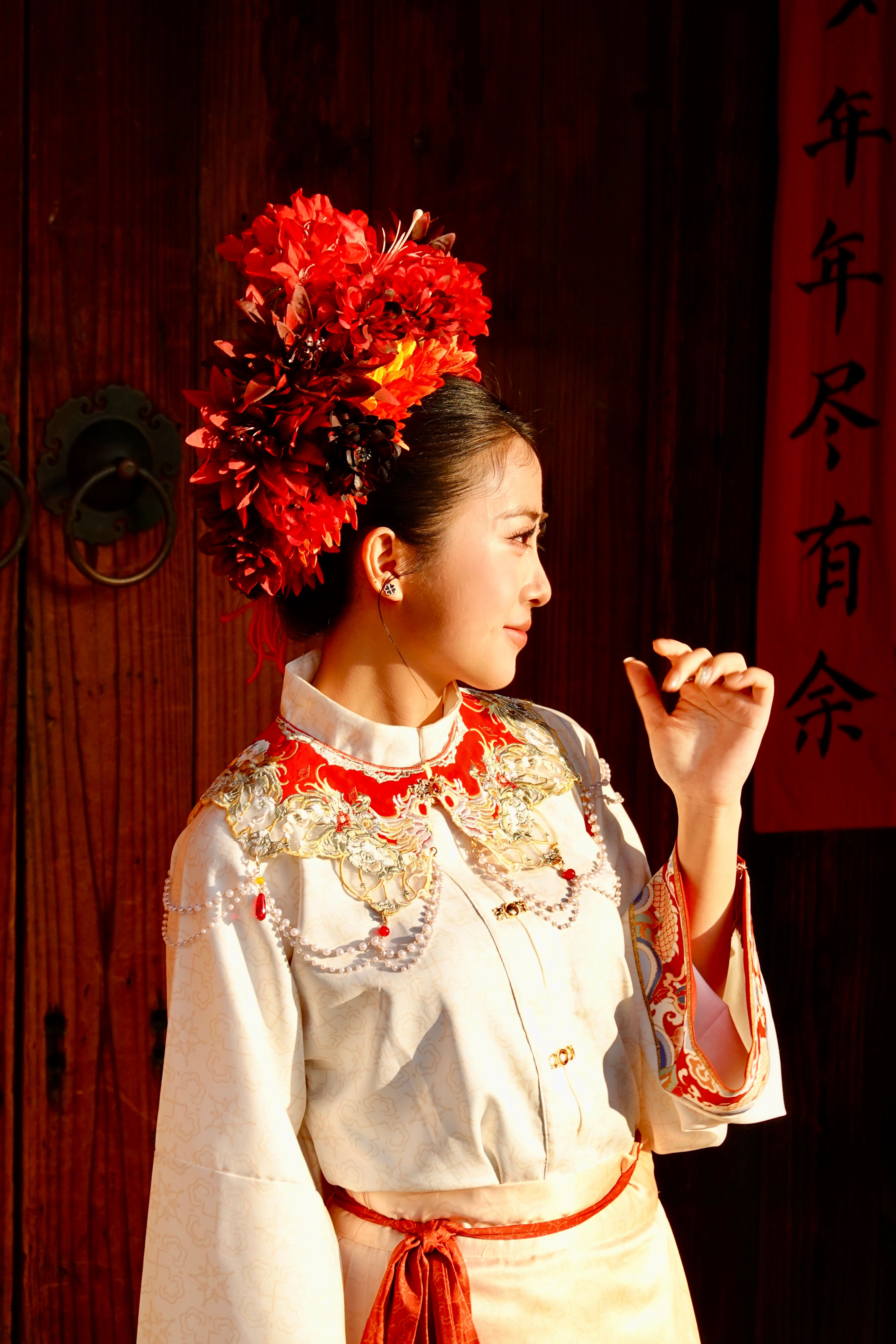 A woman in an elegant Chinese dress with intricate embroidery and a floral headdress poses thoughtfully.