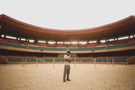 A man stands casually in the center of a vast, empty outdoor stadium in Niger.
