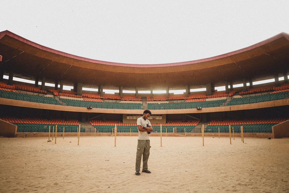 A man stands casually in the center of a vast, empty outdoor stadium in Niger.