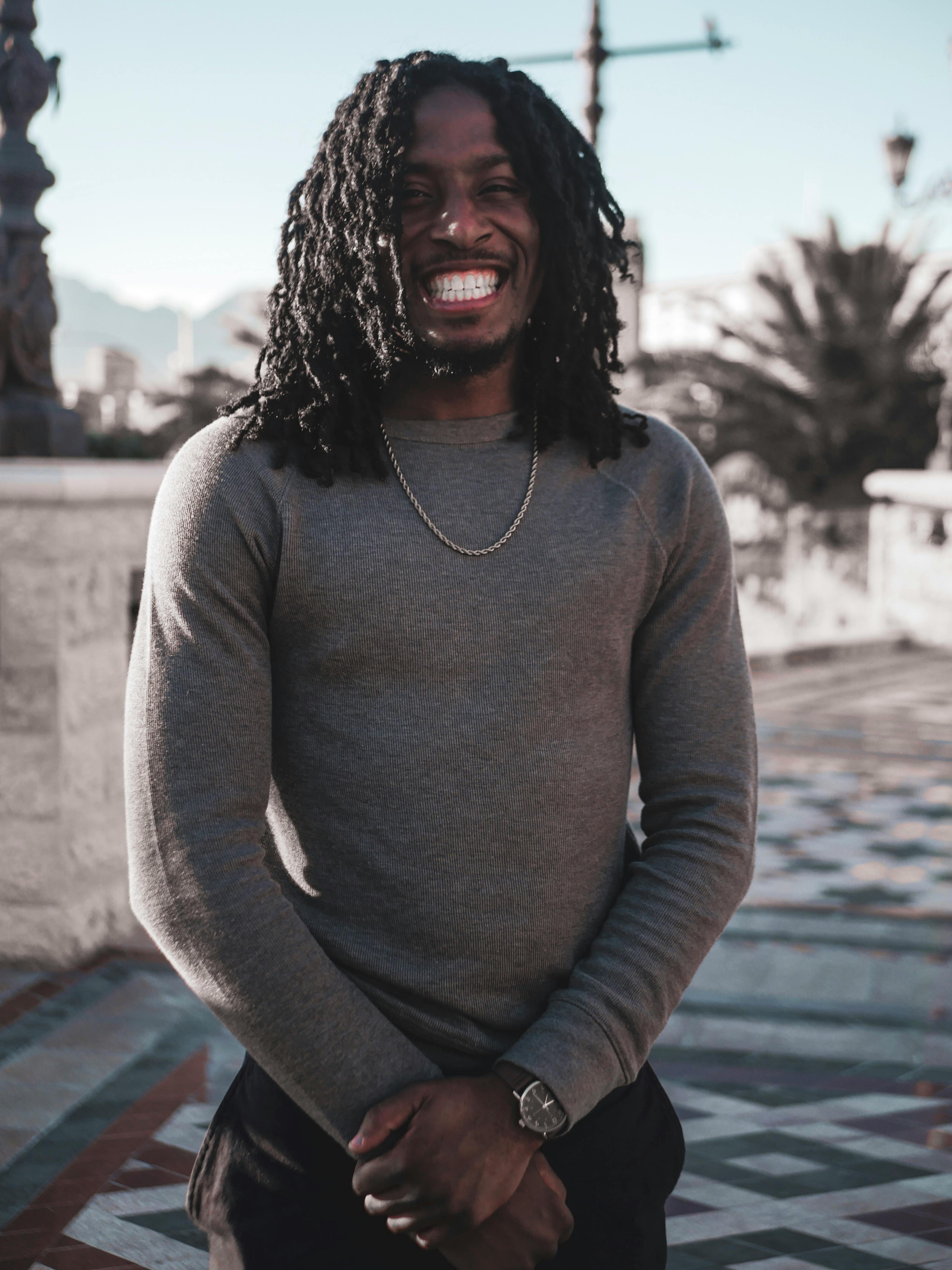 一个快乐的扎辫子男人站在铺着瓷砖的小路上，享受着户外阳光明媚的一天