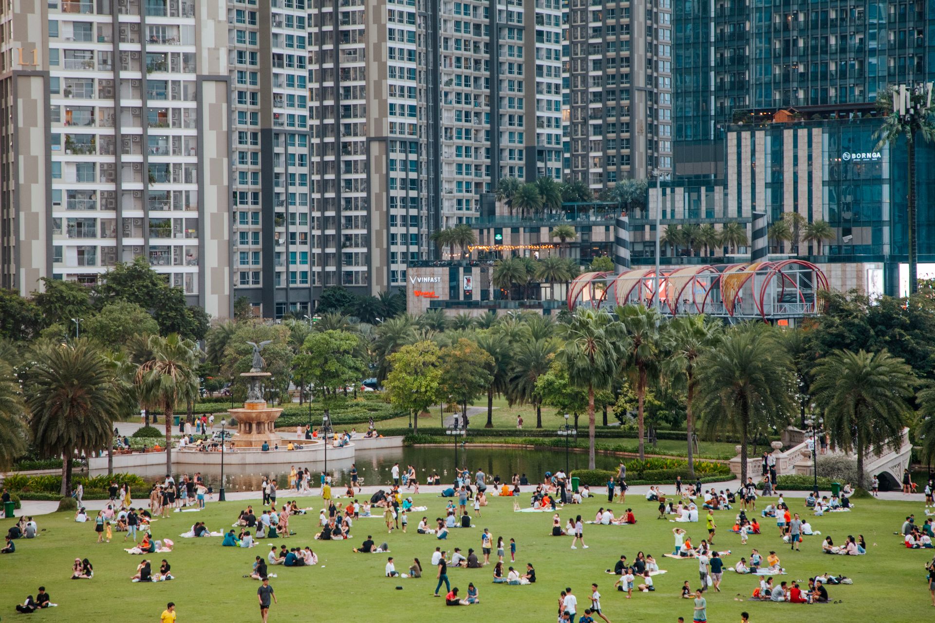 People relaxing in KLCC Park with a view of skyscrapers and a central fountain in Kuala Lumpur, Malaysia.