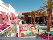 优雅的度假泳池洋溢着粉红色的活力气息，明亮的日光下，棕榈树茁壮生长