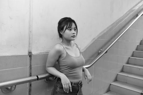 Black and White Photo of a Young Woman Standing against a Wall 