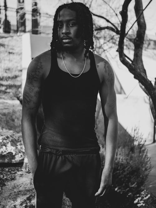 Grayscale Photography of Man in Tank Top Standing Beside Tree