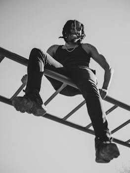 Black and white photo of a man smiling while sitting on a jungle gym outdoors.