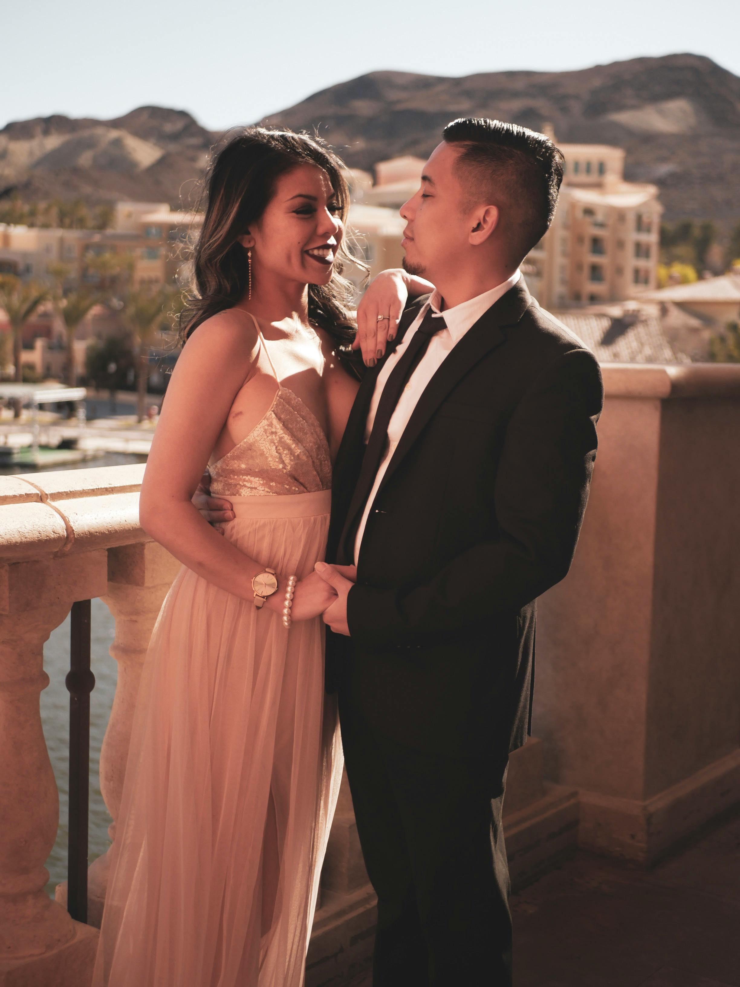 一对衣着优雅的浪漫情侣，在阳光明媚的阳台上相拥，背景是连绵的山脉