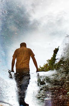 Silhouette of man in a plaid shirt reflected in a rain puddle, Kolkata, India.