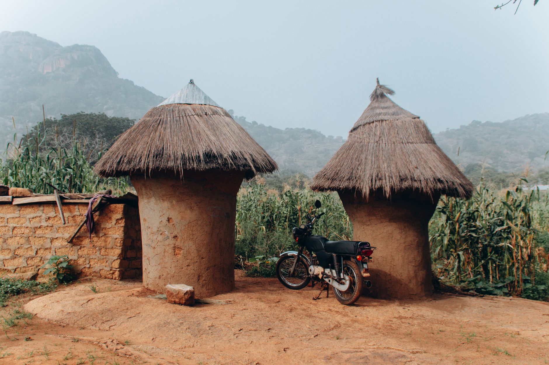 Traditional thatched huts in a rural Nigerian landscape with a motorcycle nearby.