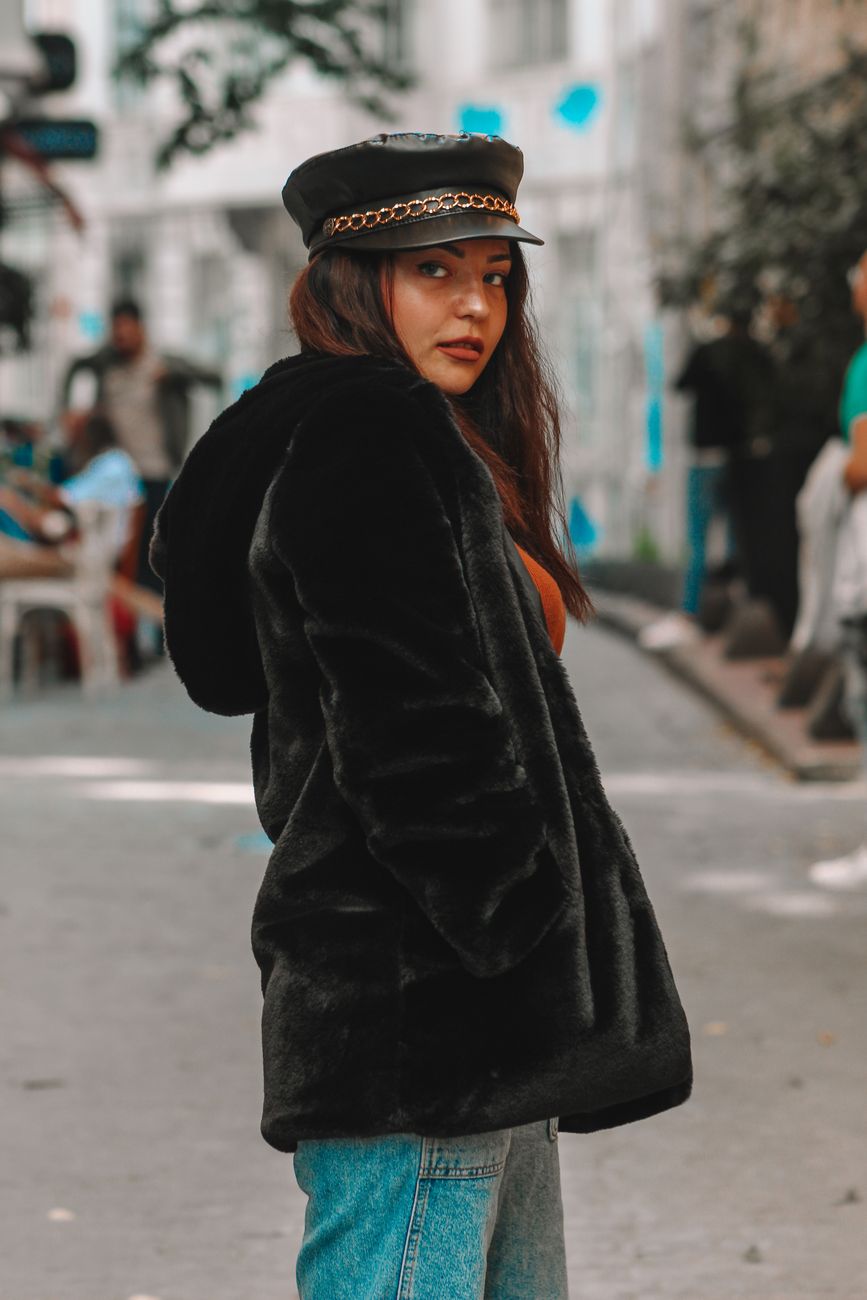 A fashionable woman in a black fur jacket poses confidently on city streets.
