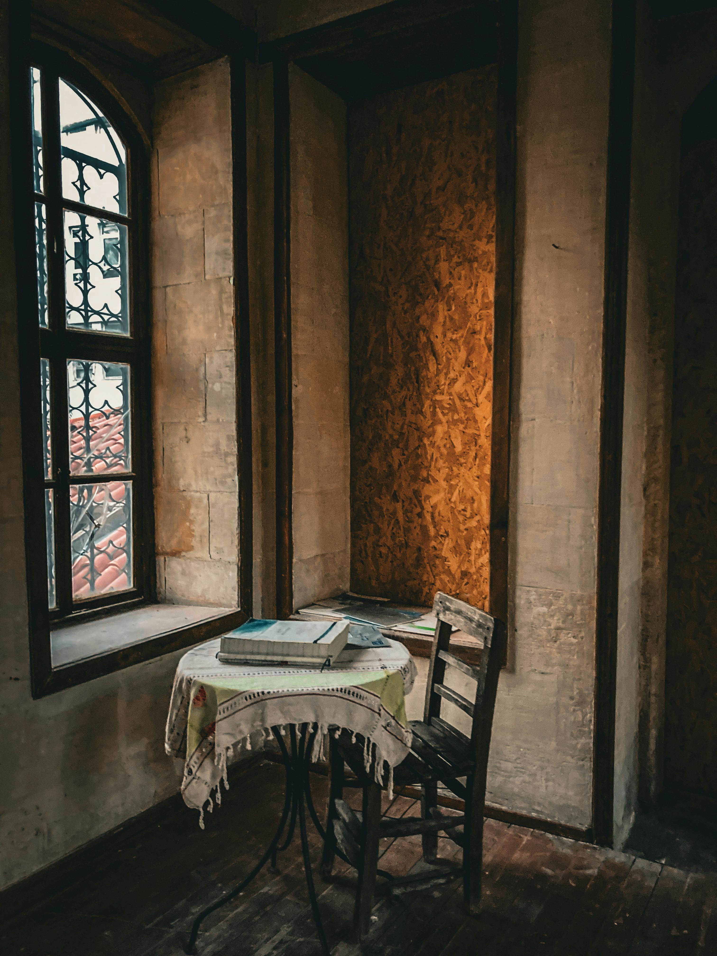 Free Cozy corner inside a historic castle with a table and chair by a window, perfect for solitude. Stock Photo