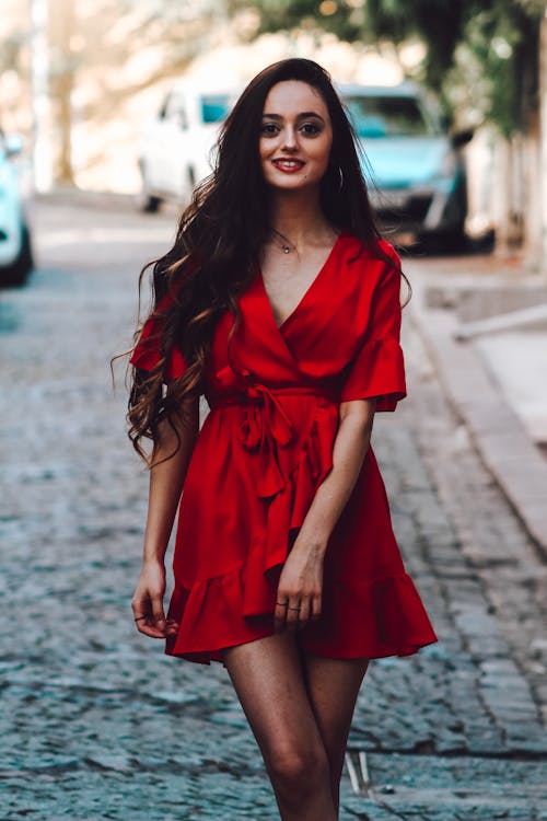 Young Woman in a Red Dress Standing on a Street and Smiling 