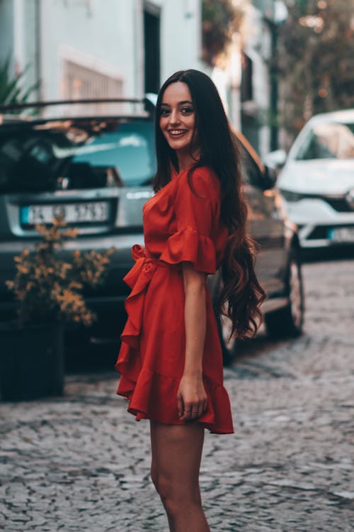 Young Woman in a Red Dress Standing on a Street and Smiling 