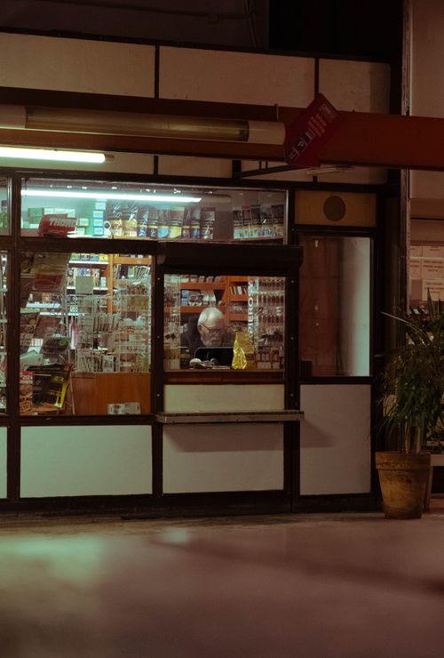Free An elderly man sits inside an illuminated store in Wrocław at night, offering a glimpse of urban life. Stock Photo