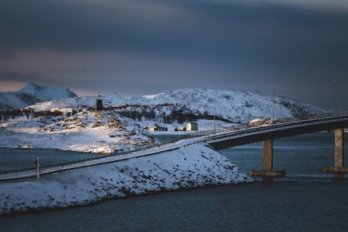 A bridge over a snowy lake with mountains in the background