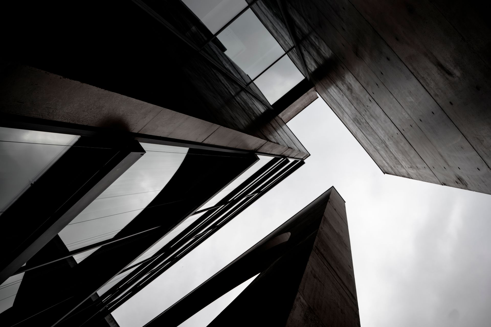 Low-angle view of dark glass and concrete towers converging against a cloudy sky