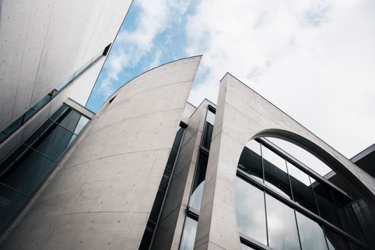 Dynamic view of modern architecture featuring glass and concrete elements under a cloudy sky.