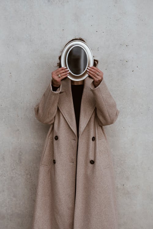 A woman in a coat holding a mirror