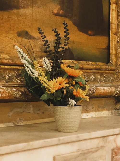 Free A vibrant floral centerpiece sits elegantly on a classic mantelpiece with an ornate golden frame. Stock Photo