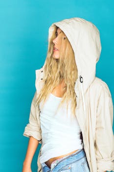 一位身穿米色连帽衫的年轻女子站在亮蓝色背景前，显得休闲时尚
