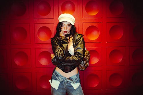A woman in a hat and jacket standing next to a red wall