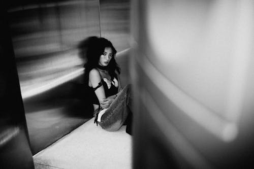 Black and White Photo of a Young Woman Sitting against a Silver Wall 