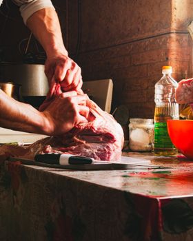 Close-up of a butcher preparing raw meat on a countertop with kitchen tools and ingredients.