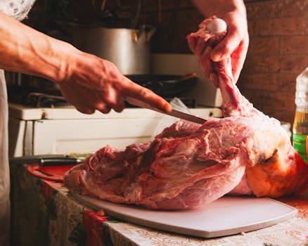 A person skillfully cutting a large piece of meat with a knife in an indoor kitchen environment.