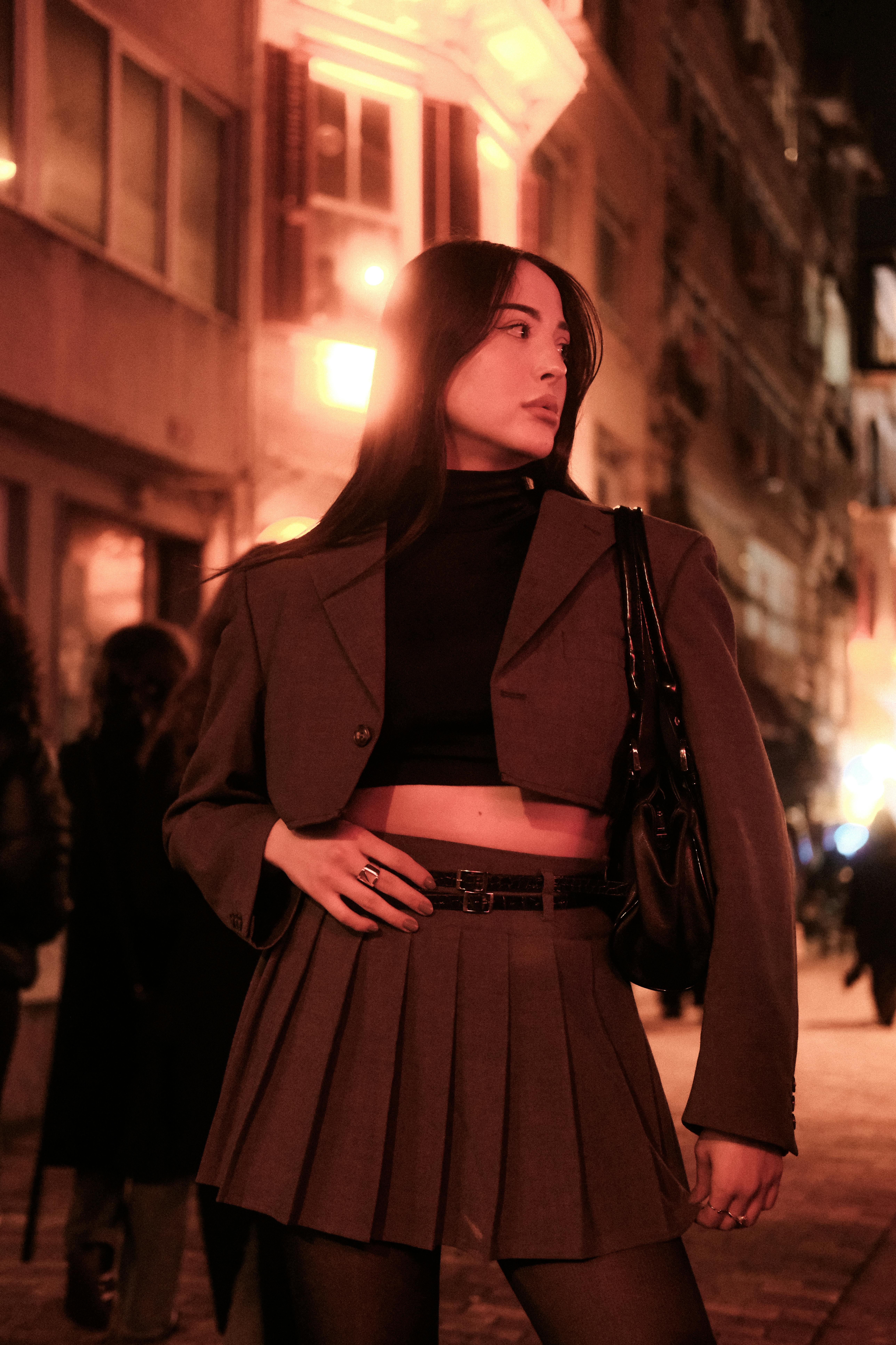Stylish young woman posing in urban setting at night, exuding elegance and confidence.