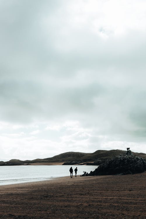 Two people walking on the beach with a cloudy sky