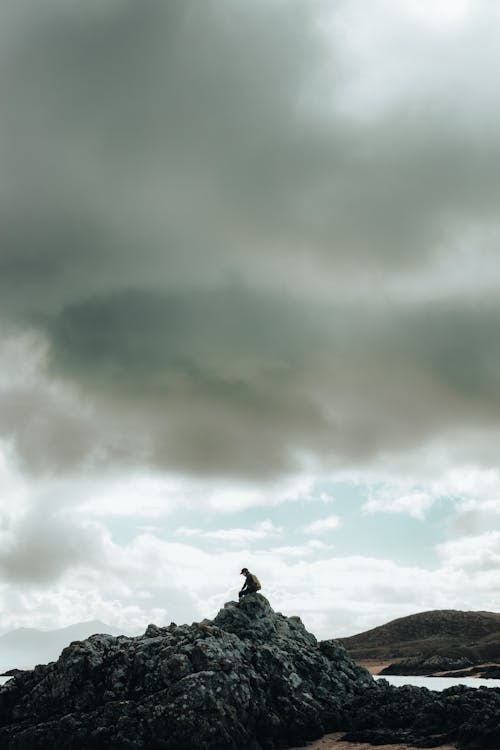 A person sitting on top of a rock with a cloudy sky