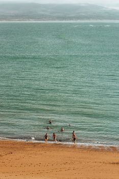 Drone shot of a serene beach with people enjoying the summer sun by the sea.