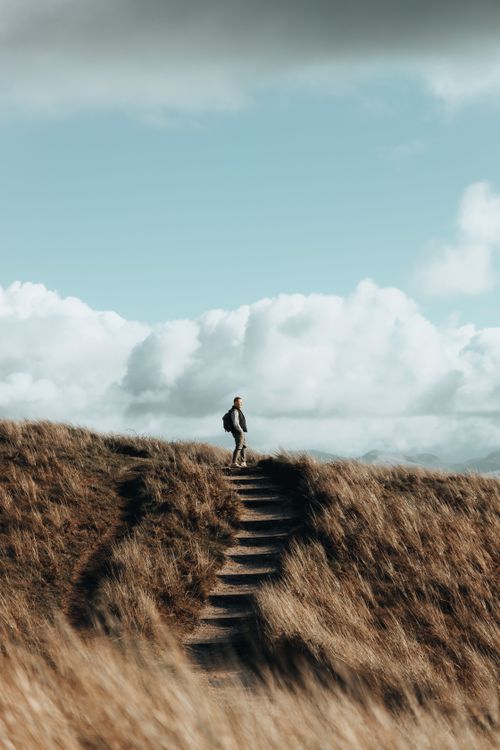 Free A lone man hiking up a grassy hill under a sky filled with dramatic clouds. Stock Photo