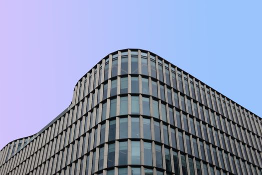 Curved glass facade of a modern building with a pastel gradient sky.