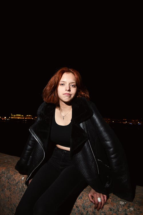 Portrait of a Young Woman Wearing a Black Leather Jacket Sitting Outdoors at Night