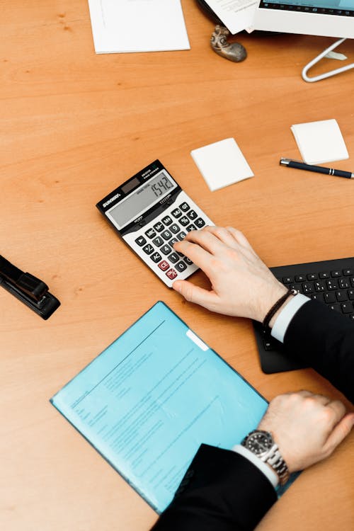 Person Using Calculator on Brown Wooden Surface