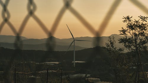 A wind turbine is seen through a chain link fence