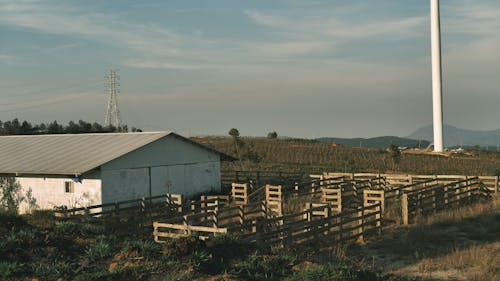 A wind turbine in the distance with a barn and fence