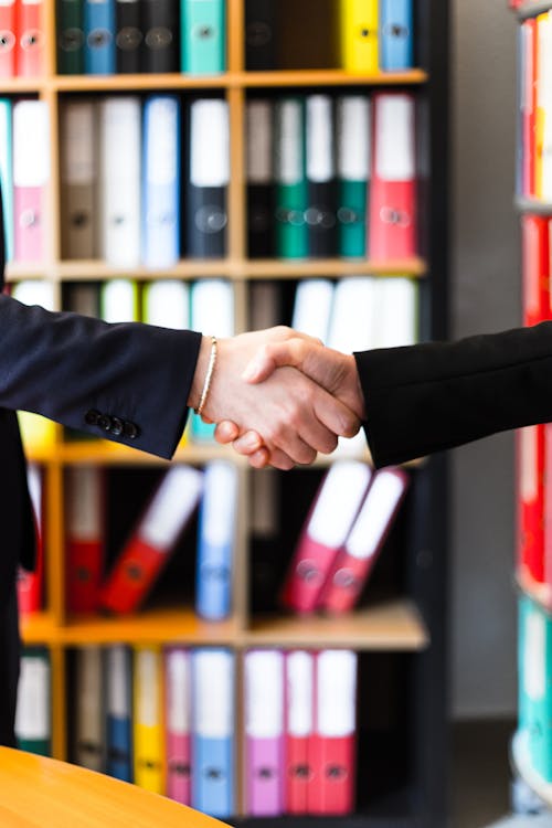 Two Person Handshakes in Front of Books on Shelf