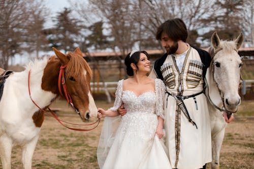 A bride and groom are standing next to two horses