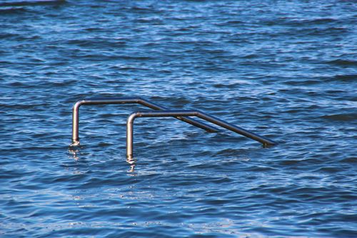 Free A tranquil lake with partially submerged metal handrails, reflecting calm water on a sunny day. Stock Photo
