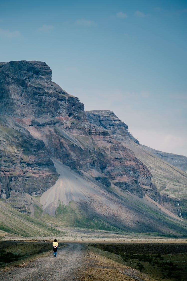 Person Walking On A Road Towards A Mountain