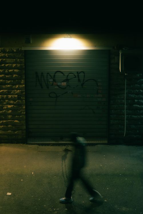 Free Nighttime urban scene featuring a blurred person walking in front of a graffitied wall. Stock Photo
