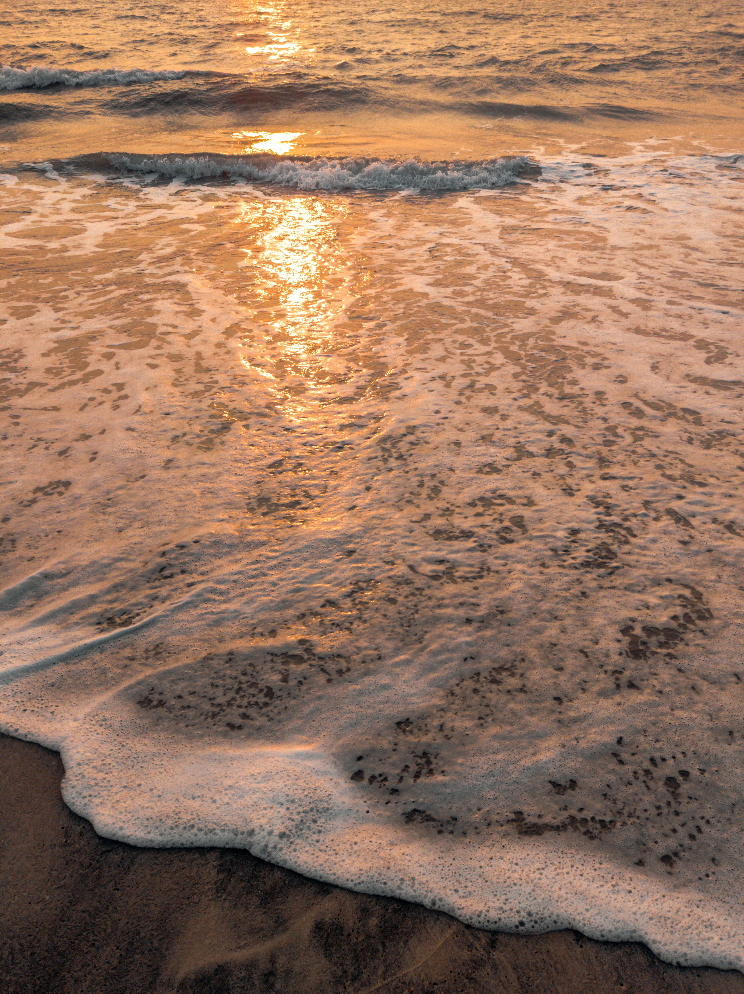 Calm ocean waves washing onto sandy beach at sunrise, creating a serene and peaceful scene.