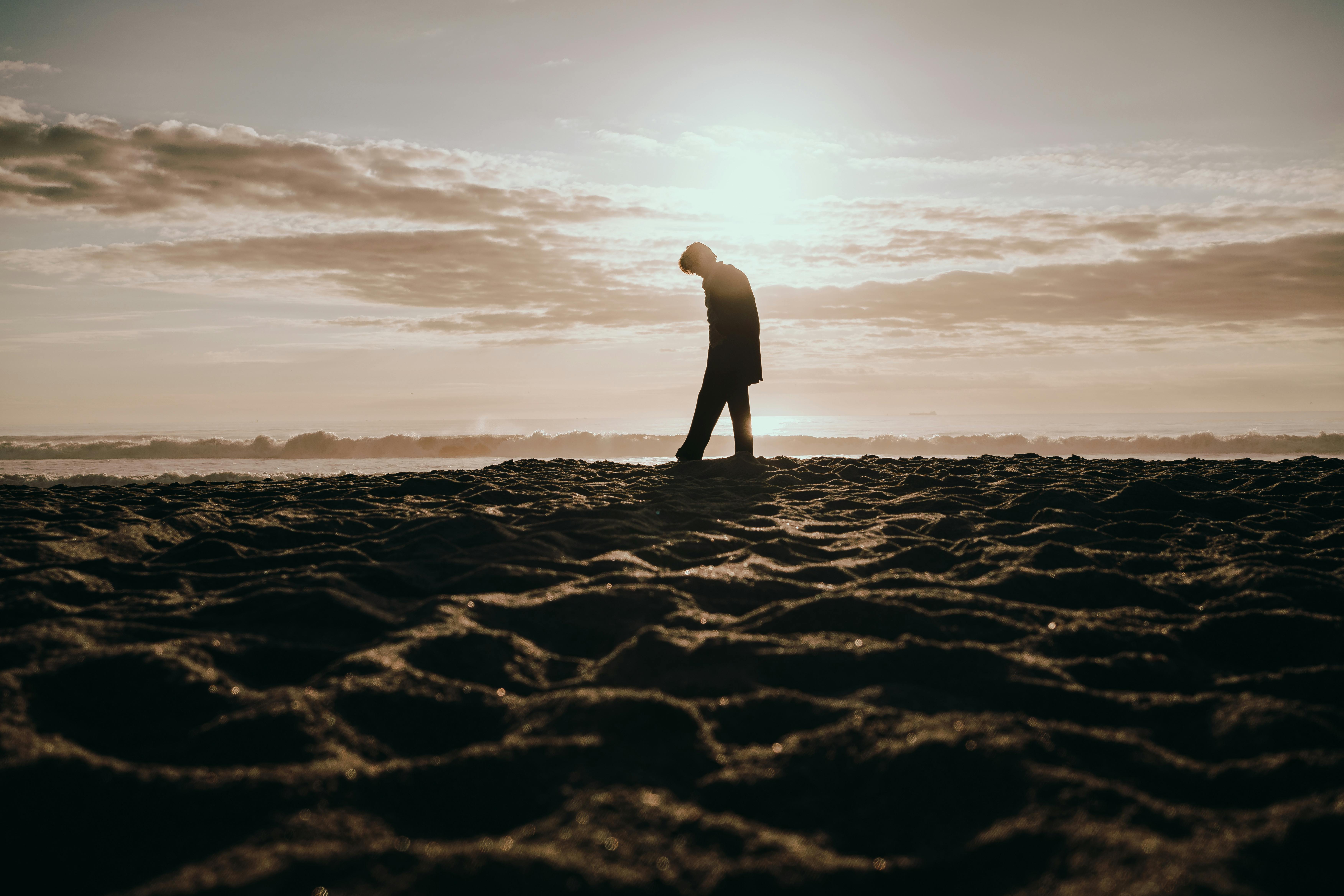 A solitary person walking along a beach at sunset, captured in a dramatic silhouette.