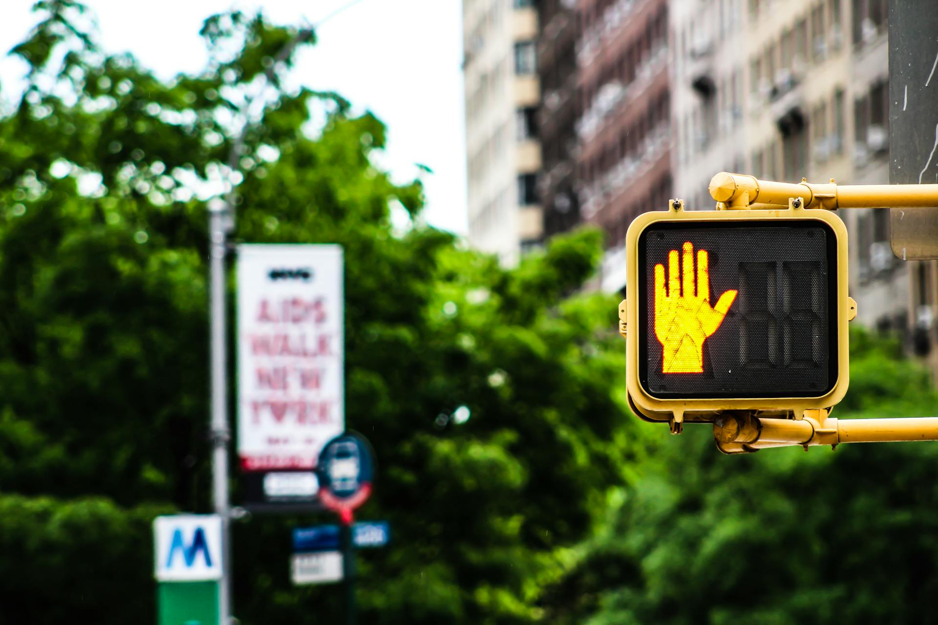 A vibrant New York City street scene featuring a pedestrian stop signal with lush greenery and buildings in the background.