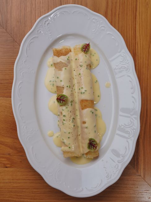 A seared ribeye steak sliced on a white plate, draped in a creamy pale sauce studded with veins of Roquefort blue cheese and topped with chopped chives, with a cast iron skillet visible in the background.