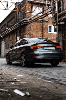 A sleek black sedan parked in an industrial urban alleyway, showcasing modern automotive design.