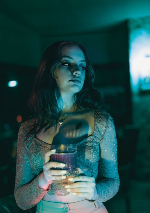 Free Capture of a woman holding a drink under vibrant blue lights in a nightclub setting. Stock Photo
