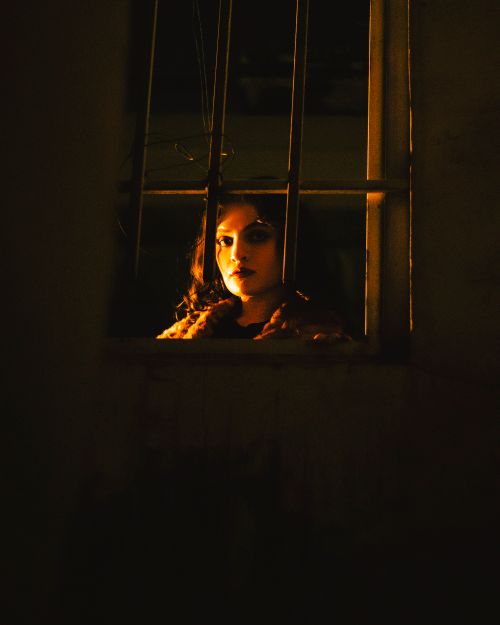 Free Mysterious portrait of a woman with dramatic lighting through metal bars at night. Stock Photo