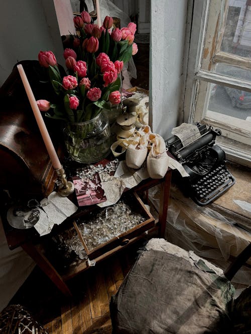 A vase of flowers sits on top of a table next to a typewriter